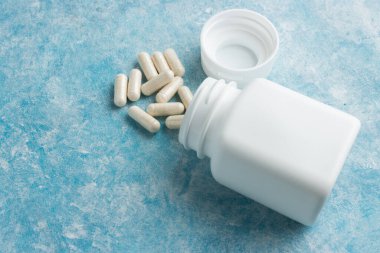 Mavi arka plan, vitamin ve mineraller, besin veya beslenme takviyesi için beyaz tıbbi kapsüller, haplar veya ilaçlar.