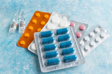 Mavi arka plan, sağlık ve tıp konsepti üzerine su toplayan bir pakette çeşitli kapsüller, haplar ve tabletler yığını.