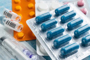 Mavi arka plan, sağlık ve tıp konsepti üzerine su toplayan bir pakette çeşitli kapsüller, haplar ve tabletler yığını.