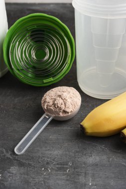 Plastik bir kaşıkta çikolata aromalı beyaz protein tozu. Arka planda, muzlu ve sallanan bir kaşık..