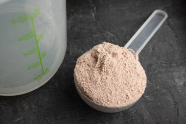 Koyu arkaplanda plastik bir kaşık içindeki çikolata aromalı beyaz protein tozu..