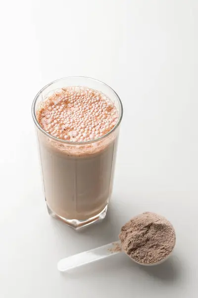 Protein drink cocktail in a glass and whey protein powder in a measuring scoop.