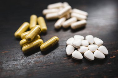 Beyaz ilaç hapları ve sarı kapsüller, ilaç tedavisi ve yakın çekim görüntüsü.