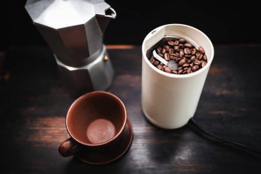 Elektrikli kahve öğütücüsünde kavrulmuş kahve çekirdekleri ahşap bir masada, kahve demliği ve kahve hazırlama..