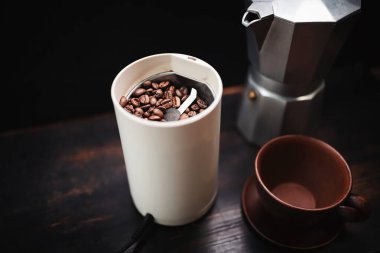 Elektrikli kahve öğütücüsünde kavrulmuş kahve çekirdekleri ahşap bir masada, kahve demliği ve kahve hazırlama..