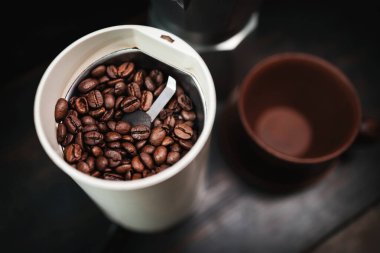 Elektrikli kahve öğütücüsünde kavrulmuş kahve çekirdekleri ahşap bir masada, kahve demliği ve kahve hazırlama..