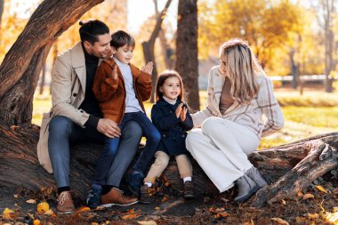 Sonbahar parkında mutlu bir aile. Anne, baba, oğul ve kız bir ağaç gövdesinde oturuyorlar.