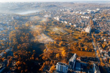 Chisinau, Moldova 'daki Dendrarium Parkı' nın hava aracı görüntüsü. Park sararmış ağaçlar ve çimlerle dolu, hava sisli, yerleşim bölgesi var.