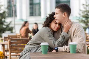 Açık havada bir kafe yakınında romantik bir çift. Sarılmak, masanın üstünde kahve içmek. Sonbahar atmosferi