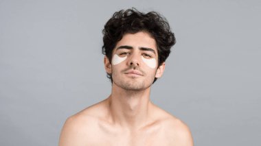 Sakallı, gözlerinin altında yamalar olan beyaz bir adam kameraya bakıyordu.