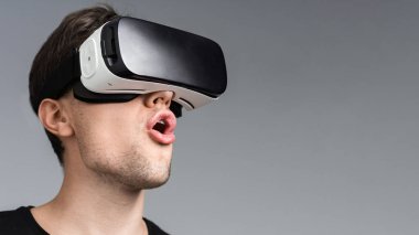 Genç bir adam VR gözlük takarken heyecanlı, gri arka plan
