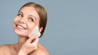 Gua Sha kullanarak yüz masajı yapan mavi gözlü beyaz bir kadın.