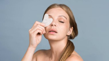 Gua Sha ile yüz masajı için poz veren beyaz bir kadın.