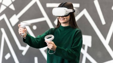 VR oyunlarıyla ilgilenen genç bir kadın VR gözlüğü ve kumanda kullanıyor.