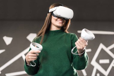 VR oyunlarıyla ilgilenen genç bir kadın VR gözlüğü ve kumanda kullanıyor.