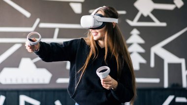 VR oyunlarıyla ilgilenen genç bir kadın VR gözlüğü ve kumanda kullanıyor.