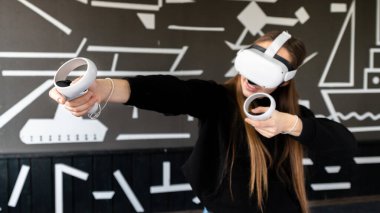 VR oyunlarıyla ilgilenen genç bir kadın VR gözlüğü ve kumanda kullanıyor.