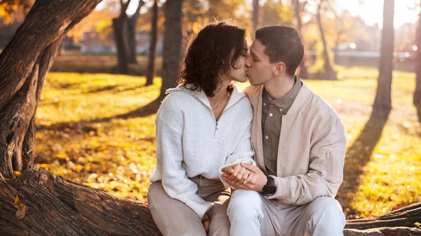 一对浪漫的夫妇在秋天的公园 坐在树干上 牵着手亲吻 秋天的空气 黄树成荫 树叶四散 — 图库照片