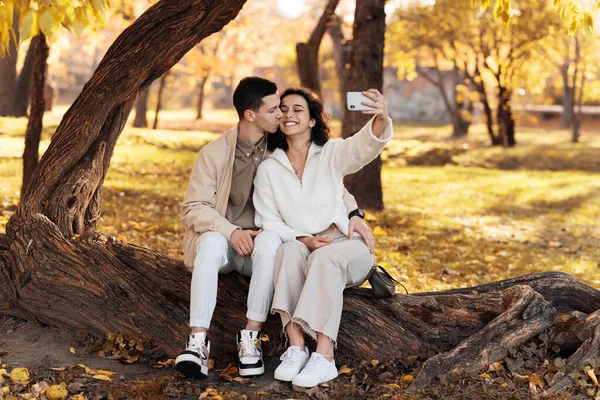 Romantyczna Para Jesiennym Parku Siedząc Pniu Drzewa Uśmiechając Się Robiąc — Zdjęcie stockowe