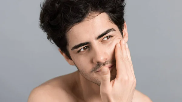 stock image A young caucasian man with stubble beard is moisturizing face and skin with cosmetic oil while doing a facial massage