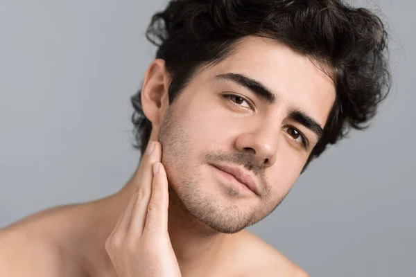 stock image A young caucasian man with stubble beard is moisturizing face and skin with cosmetic oil while doing a facial massage, looking into the camera