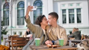 Bir kafede mutlu bir çift. Selfie çekiyorlar, öpüşüyorlar, masada kahve içiyorlar, köpekleri yakınlarda. Sonbahar atmosferi. Yavaş çekim
