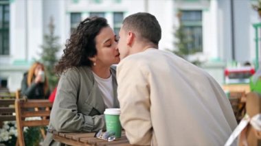 Açık havada bir kafe yakınında romantik bir çift. Öpüşme, masada kahve. Sonbahar atmosferi. Yavaş çekim