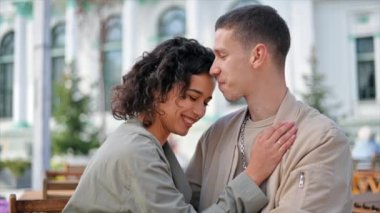 Açık havada bir kafe yakınında romantik bir çift. Kadının biri adamın omzuna uzanmış, gülümsüyor. Sonbahar atmosferi. Yavaş çekim