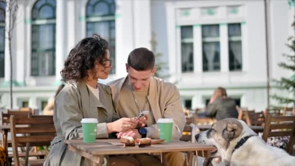 一对快乐的夫妇在外面的咖啡店附近 咖啡在桌子上 他们的狗在附近 秋天的气氛 — 图库视频影像