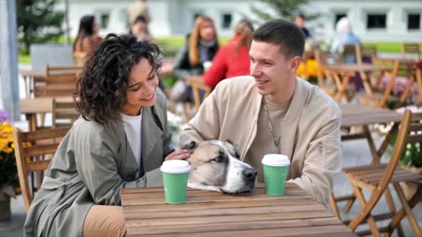 一对快乐的夫妇在外面的咖啡店附近 爱抚他们的狗 咖啡放在桌上 秋天的气氛慢动作 — 图库视频影像
