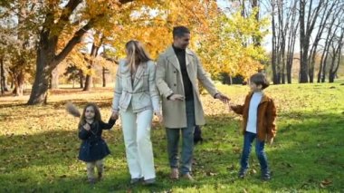 Sonbahar parkında mutlu bir aile. Anne, baba, oğul ve kız etrafta sararmış ağaçlarla konuşuyor ve yürüyor. Yavaş çekim