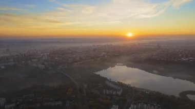 Chisinau 'nun güneş doğarken Moldova' daki hava aracı görüntüsü. Valea Morilor Parkı 'nın gölü ve sararmış ormanı, etrafında birden fazla bina, havada sis.