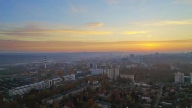 Chisinau 'nun güneş doğarken, Moldova' daki hava aracı görüntüsü. Gökyüzü sisli şehir manzarası, birden fazla meskun bina, meydan ve caddelerde sararmış ağaçlar.