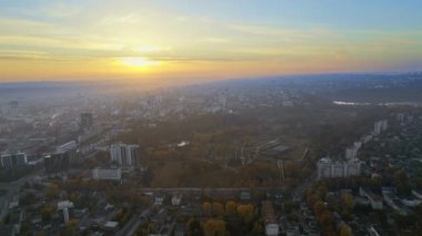 Chisinau 'nun güneş doğarken, Moldova' daki hava aracı görüntüsü. Gökyüzü sisli şehir manzarası, birden fazla meskun bina, Dendrarium parkı ve sarı ağaçlı sokaklar.