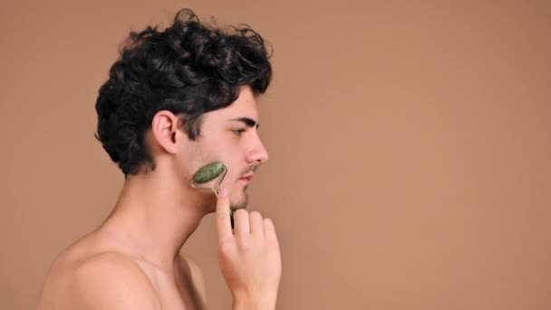 顎髭を生やした若い白人男性がローラーを使って顔のマッサージをしています — ストック動画