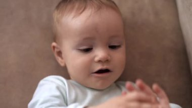 Kanepede uzanmış küçük bir çocuk, ellerine ve çevresine bakıyor, iletişim kuruyor.