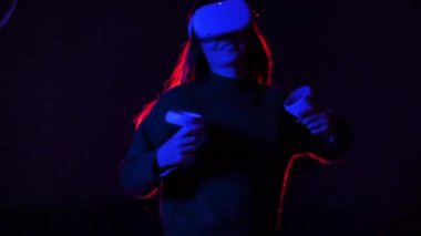 VR gözlük ve kumanda kullanarak VR oyunlarında oynayan genç bir kadın, kırmızı ve mavi ışıklandırma. Yavaş çekim