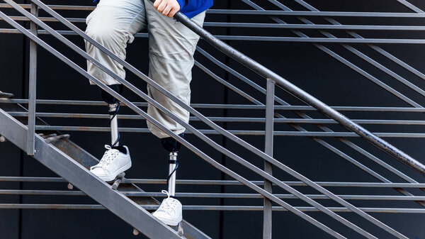 Вид человека с протезными ногами и белыми кроссовками, стоящего на металлической лестнице