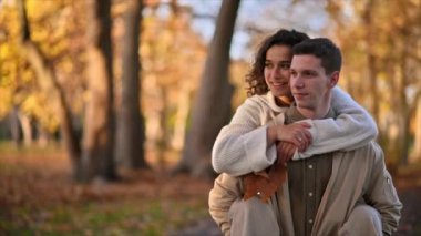 Sonbahar parkında romantik bir çift. Kadın bir şey gösterirken, sırtüstü kadını sırtında taşıyan, gülümseyen ve öpüşen bir adam. Sonbahar atmosferi, sarı ağaçlar ve yapraklar