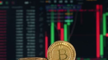 Arka planda hareket eden dijital çizelgeleri olan çoklu fiziksel Bitcoinlerin yakın görünümü