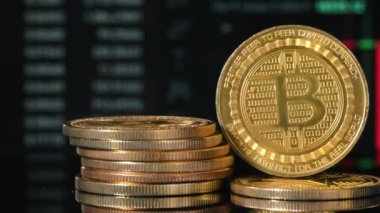 Arka planda hareket eden dijital çizelgeleri olan çoklu fiziksel Bitcoinlerin yakın görünümü