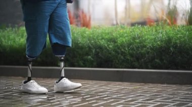 Protez bacaklı, yağmurlu havada beyaz spor ayakkabılı, arka planda yeşillik olan yürüyen bir adam görüntüsü