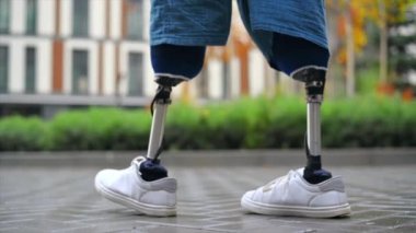 Protez bacaklı, yağmurlu havada beyaz spor ayakkabılı, arka planda yeşillik olan yürüyen bir adam görüntüsü