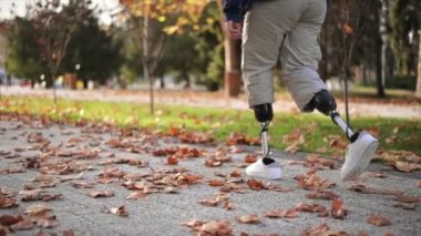 Yürüyen, protez bacaklı ve parkta beyaz spor ayakkabılı bir adamın yavaş çekim görüntüsü. Yere düşen sarı yapraklar