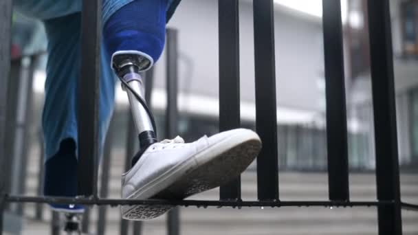在雨天看到一个穿着假腿和白色运动鞋的男人 一只脚踩在栅栏上 — 图库视频影像
