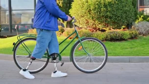看到一个有假肢的男人骑着自行车走在绿树成荫的大街上 — 图库视频影像