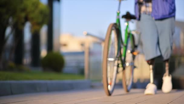 一个假肢男子的慢镜头 在街上骑着自行车走着 然后停下来 失去了注意力 — 图库视频影像