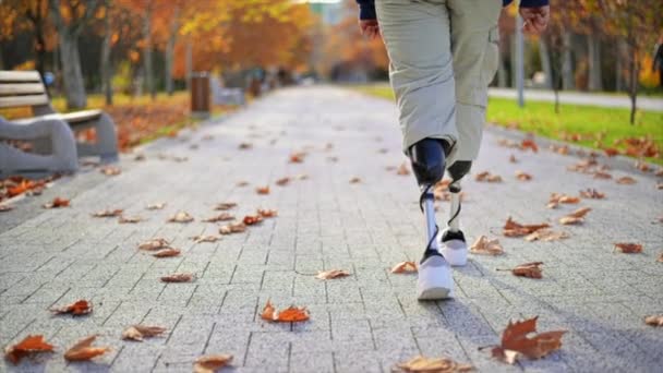 公園で義足の歩行者と白いスニーカーのスローモーションビュー 地面に落ちた黄色の葉 — ストック動画