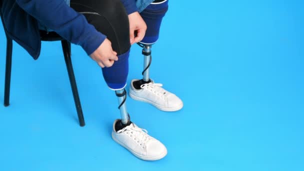 義足の男と白いスニーカーの眺め 椅子に座っている間に義肢を削除 青の背景 — ストック動画