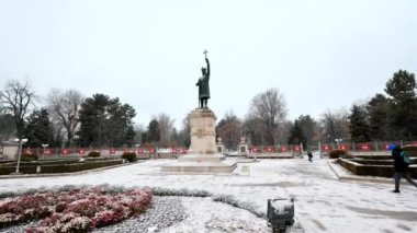 View of Stephen the Great monument during a snowfall in Chisinau, Moldova. Walking people, bare trees